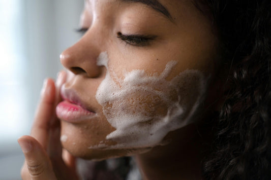 A close-up shot of a person gently washing their face, with a soft white cleanser foaming on their cheek, illustrating the 'Cleanse' step of a K-Beauty routine.